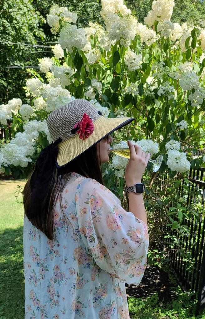 Side profile of a women drinking out of a champagne flute with a big hat on