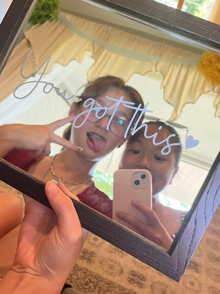 Two young girls taking a mirror selfie with the mirror that says you got this