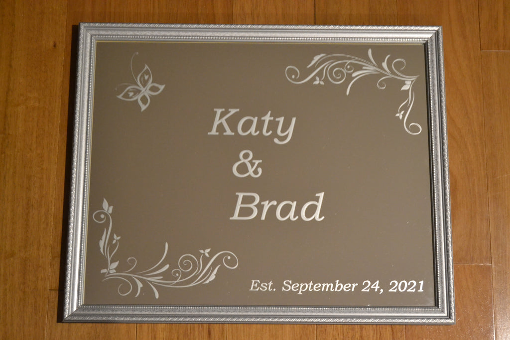 Customer mirror with a butterfly and border that have the saying "Katy and Brad Est. September 24, 2021" etched on 