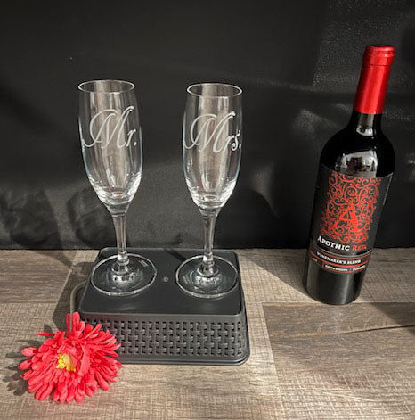 Two champagne flutes that have Mr. and Mrs. etched on standing on a basket with a wine glass next to it 