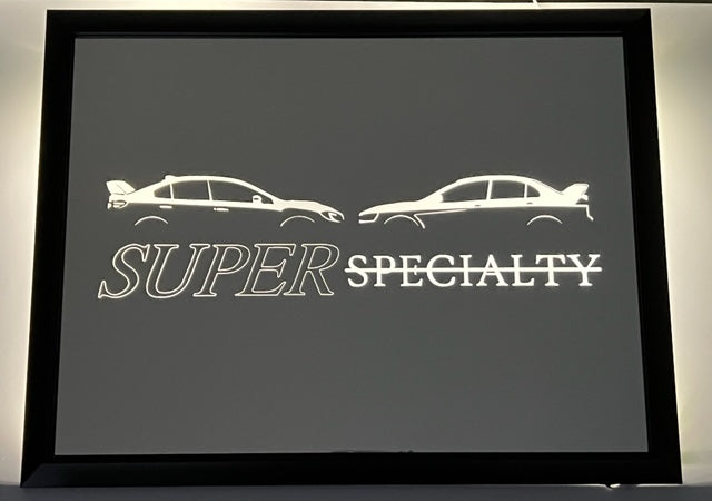 Mirror with two cars and says "super specialty" with a black frame. The picture is etched and specialty has a line through it.