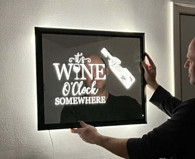 mirror that says "its wine O'clock somewhere" with a wine bottle etched on with a black frame lit up with LED lights 